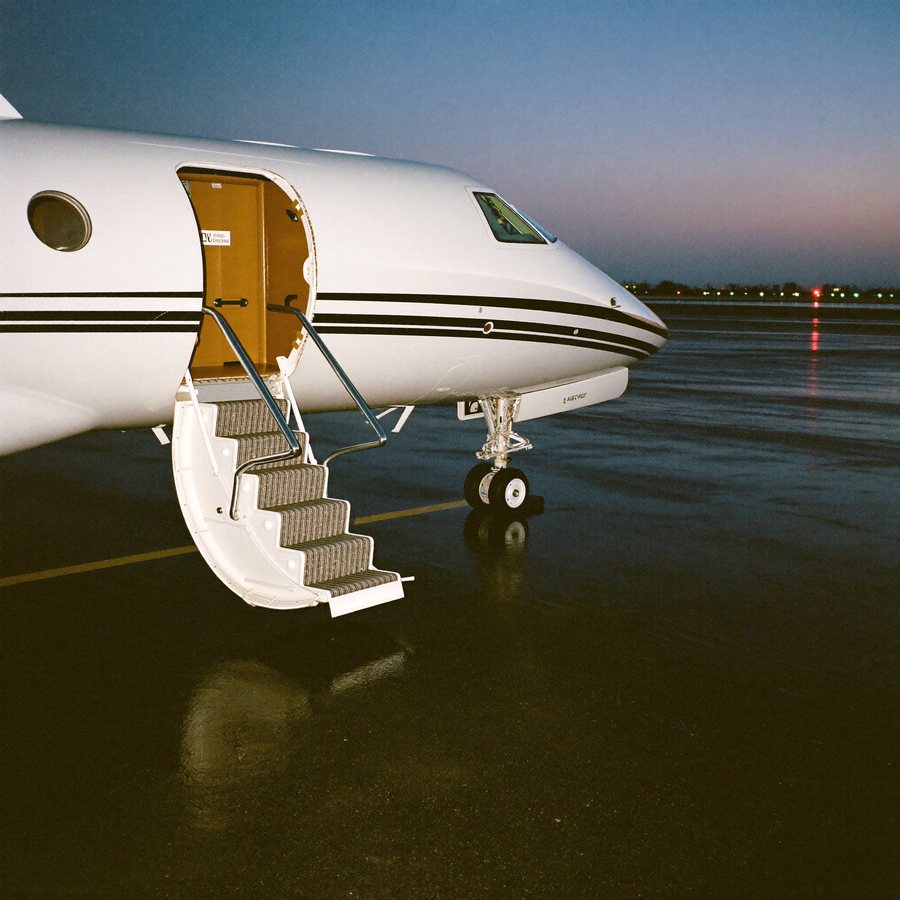 A private jet airstair on wet tarmac at dusk.