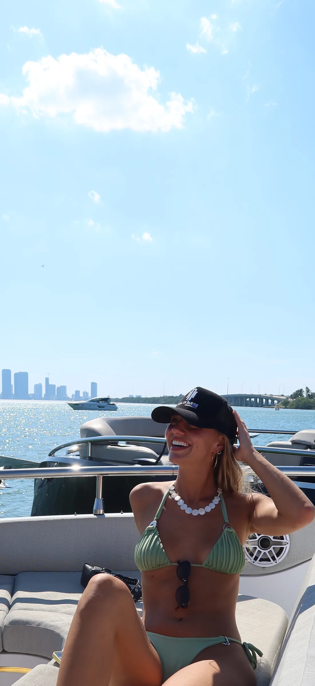A guest in an All In House cap on the bow, the downtown Miami skyline behind her.