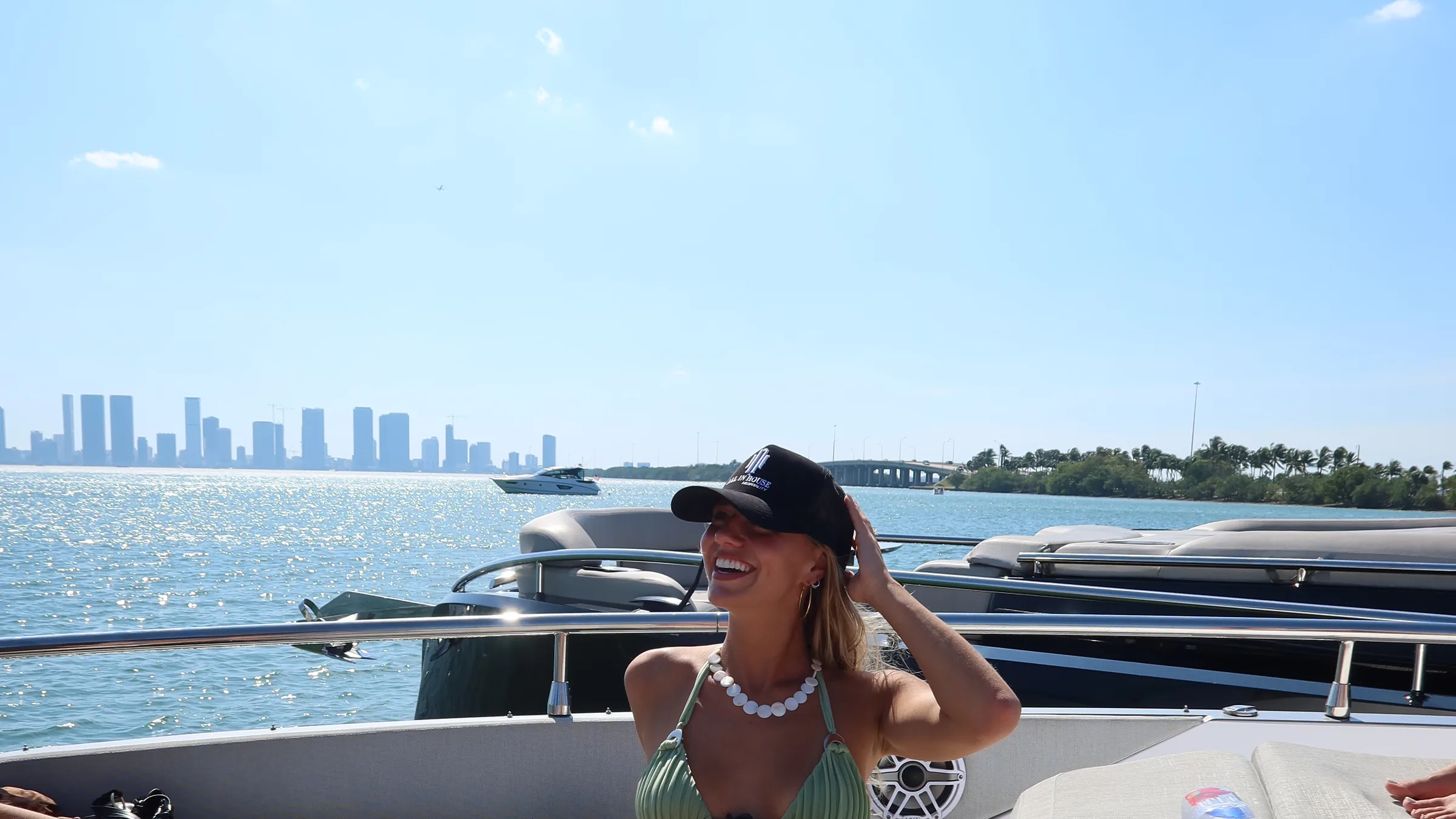 A guest in an All In House cap on the bow, the downtown Miami skyline behind her.