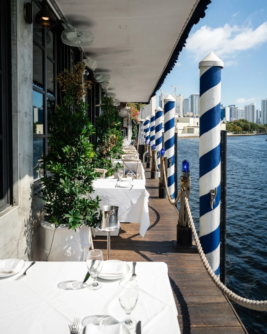 A laid table on the river terrace at Kiki, boats moored alongside.