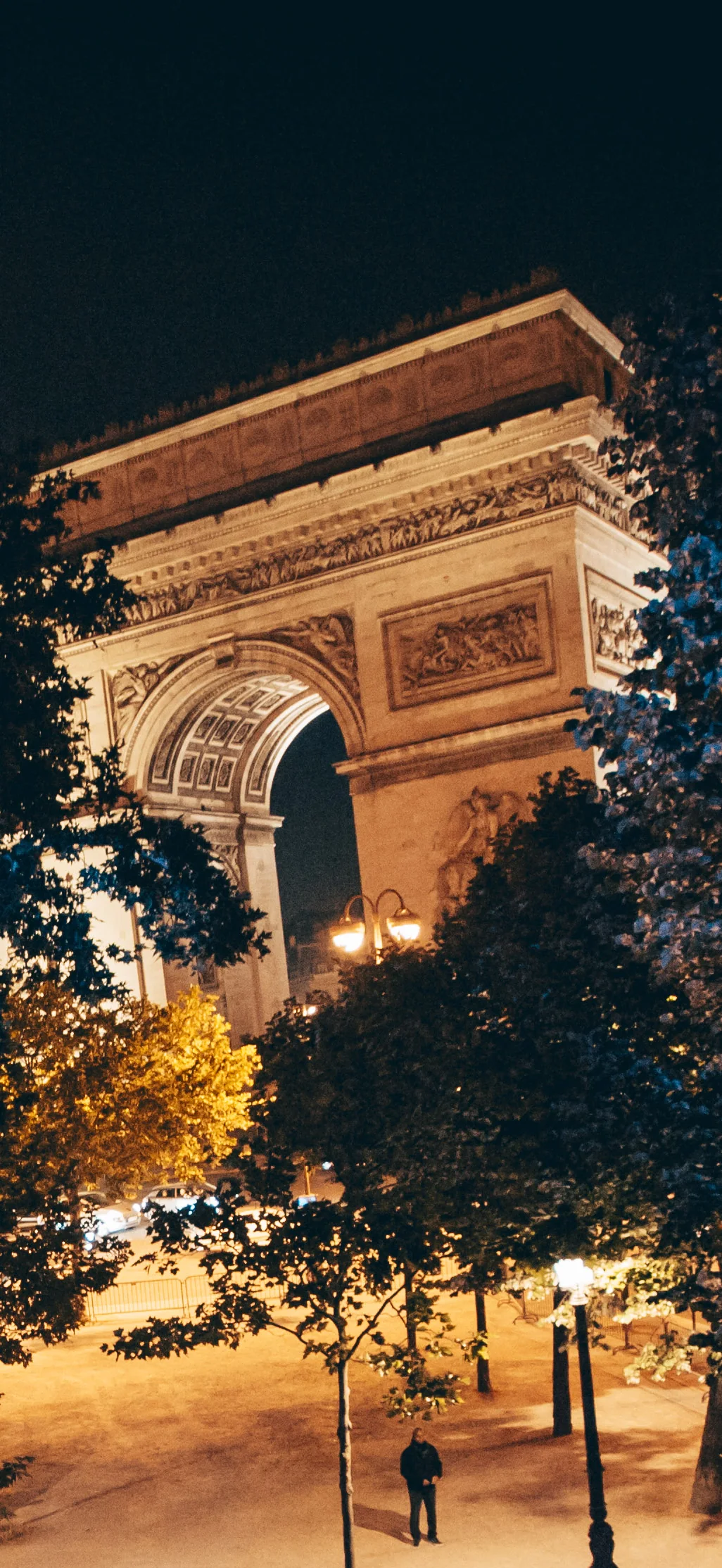The Arc de Triomphe lit at night above the trees of the avenue, from L'Arc's terrace.