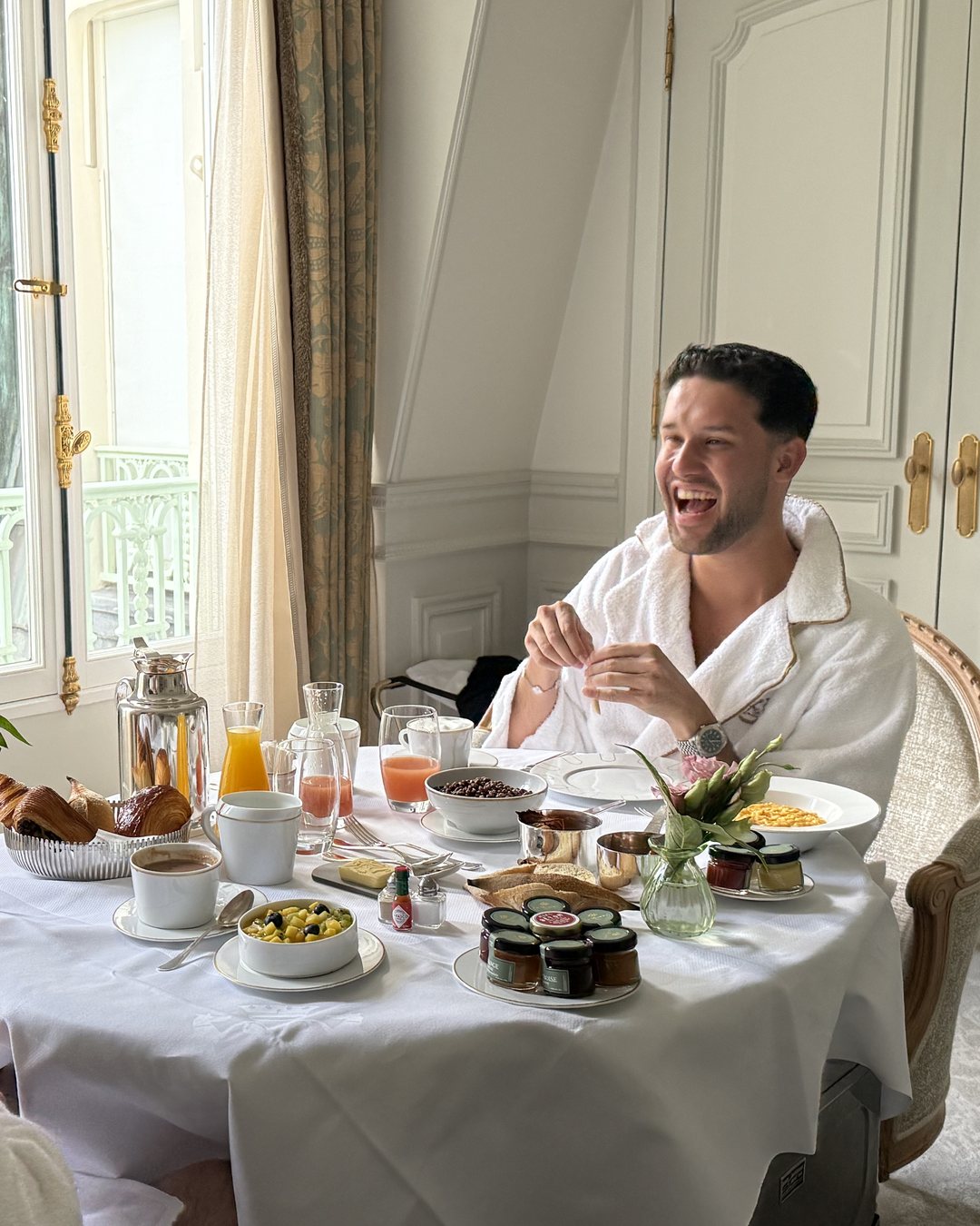 A guest laughing over breakfast, a silver coffee pot on the table.