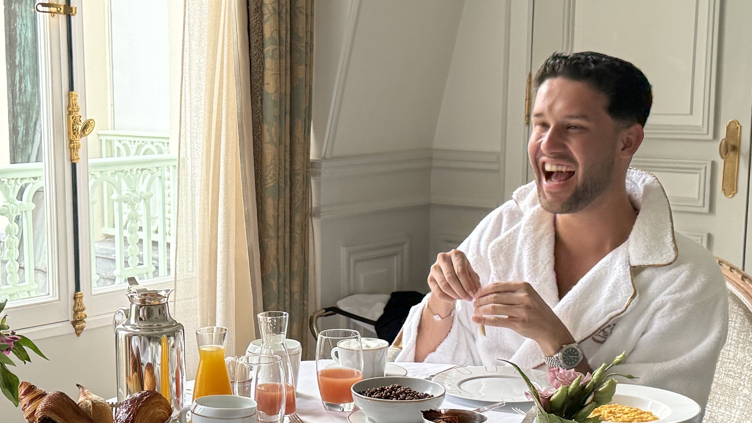 A guest laughing over breakfast, a silver coffee pot on the table.