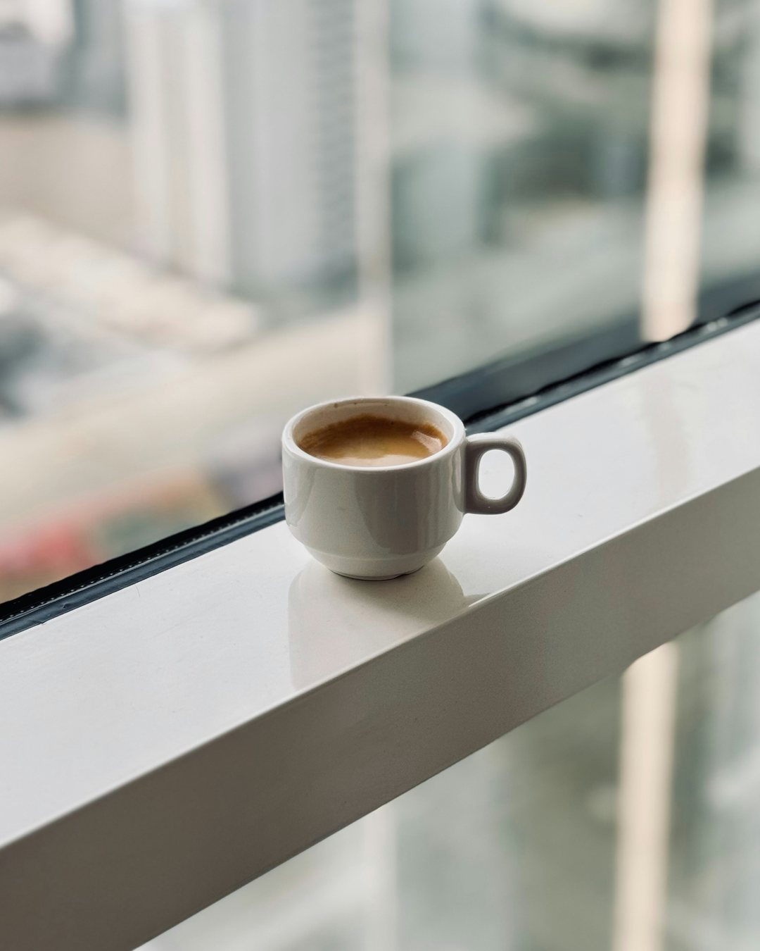 An espresso on the ledge of a high window, the city far below.
