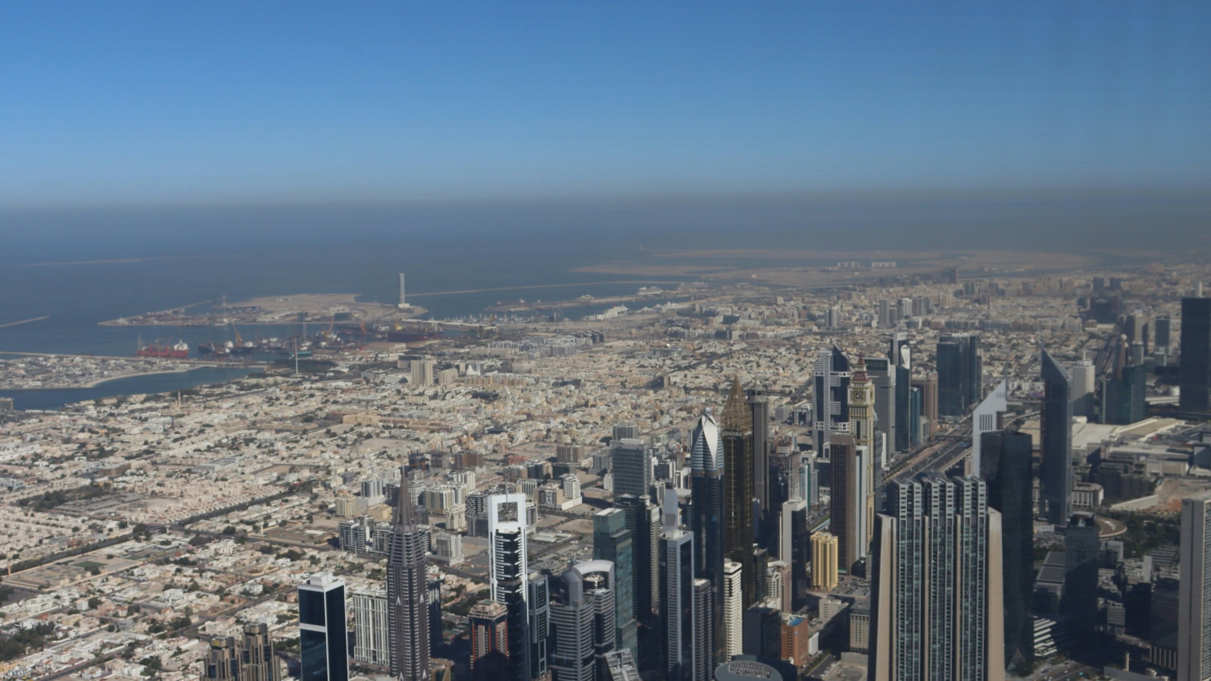 Dubai from high above Downtown on a clear day, the Gulf on the horizon.