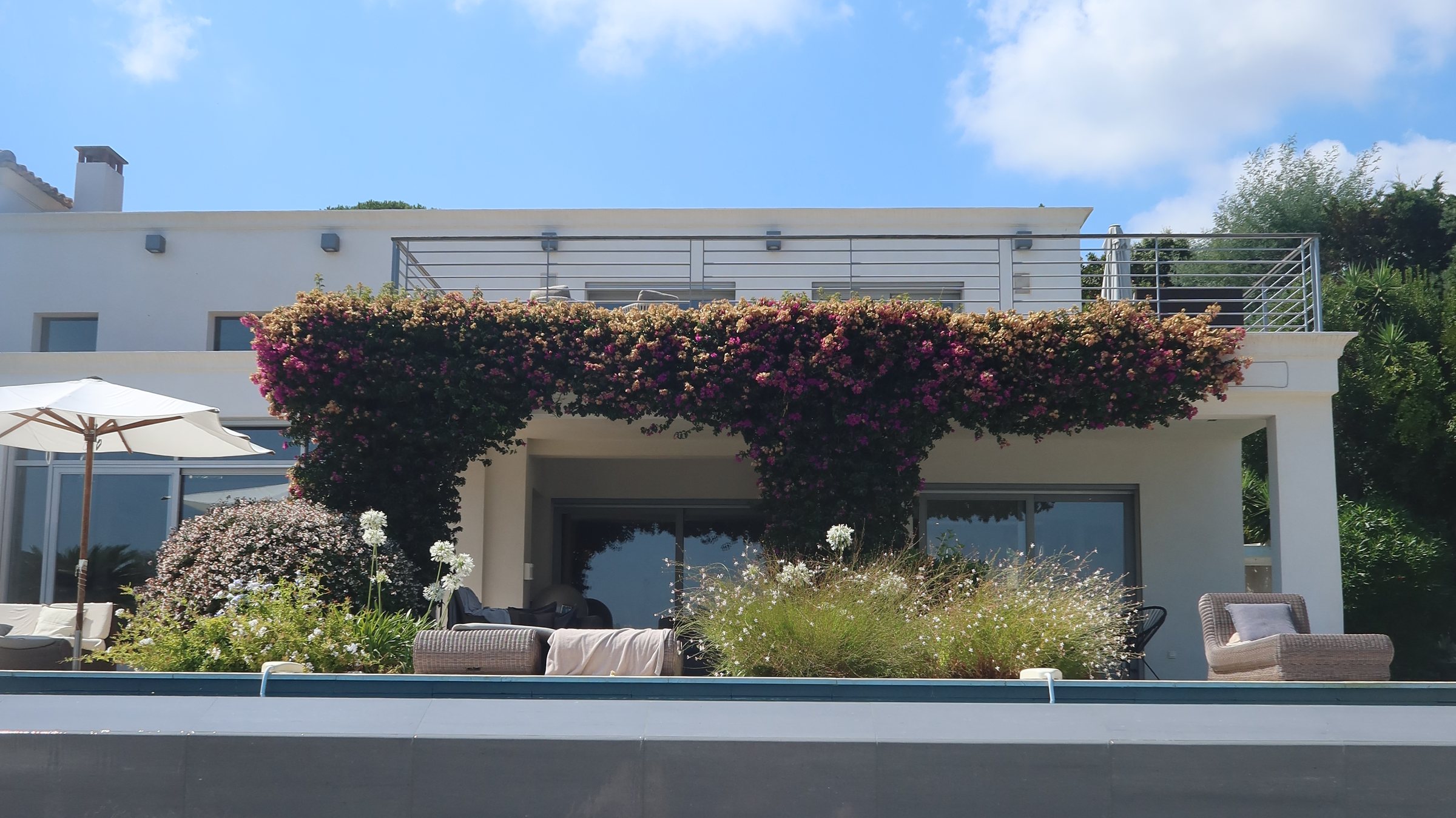 A white villa with a bougainvillea pergola above its pool.