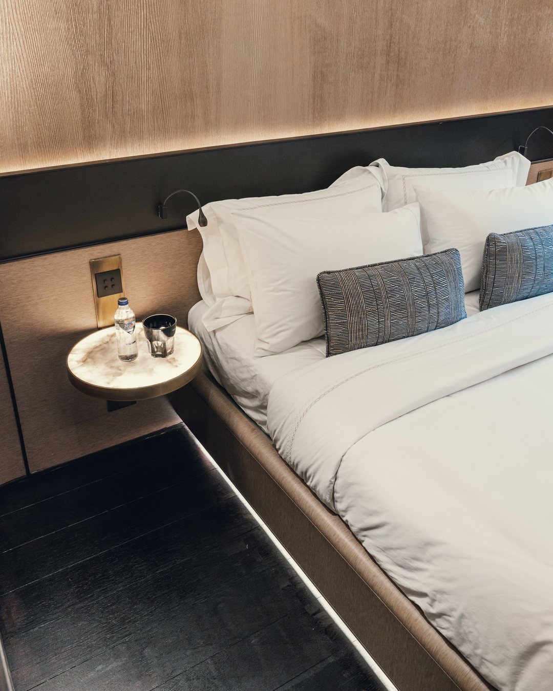 A made bed with white linen; cool blue and warm amber light drift slowly across it.