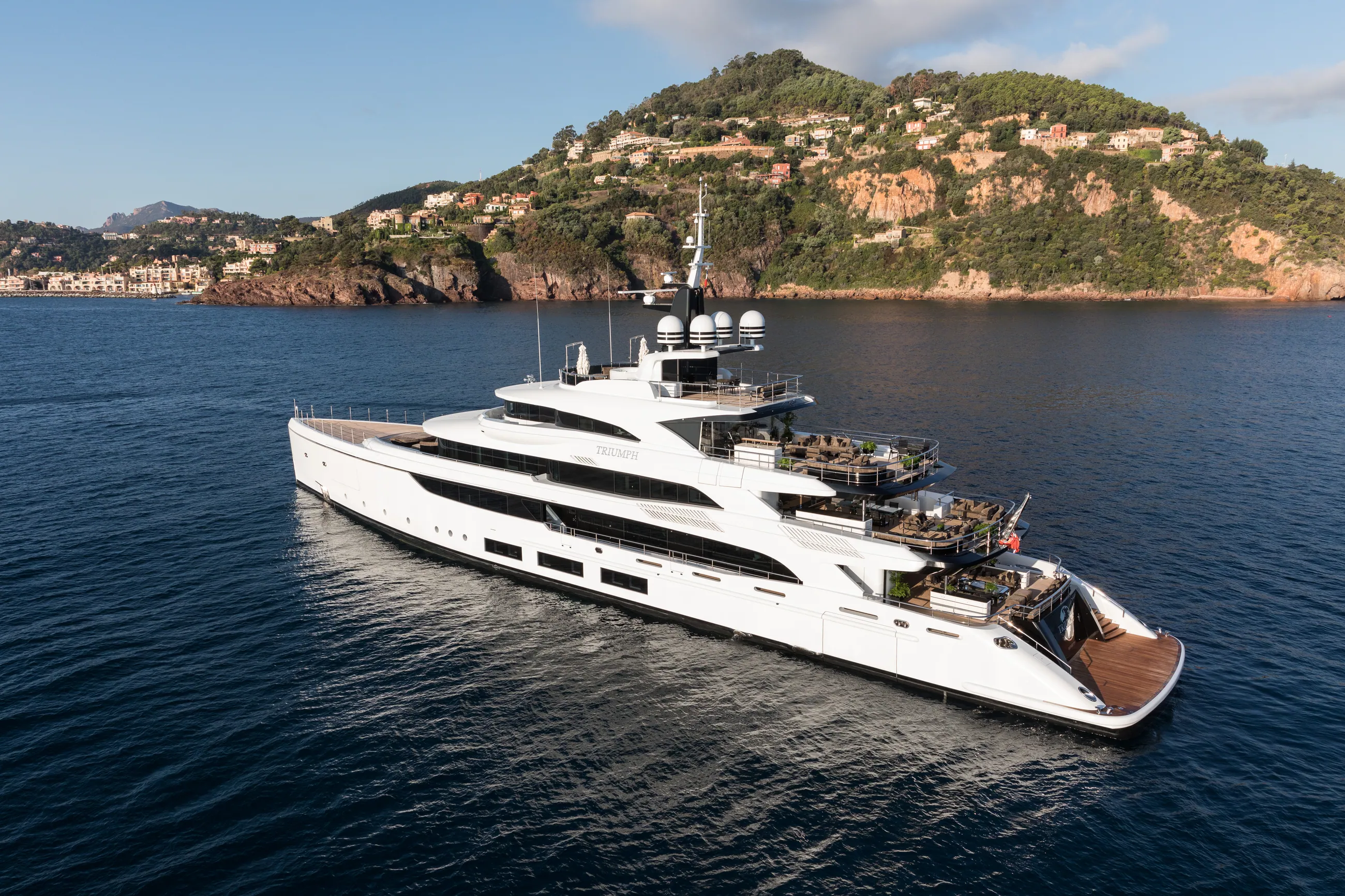 TRIUMPH at anchor below the red rock of the Esterel, late sun.